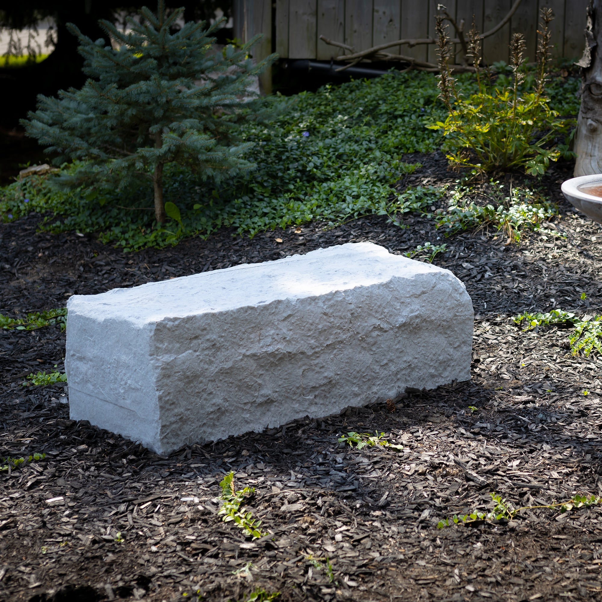 large landscape rock in grey in a woodchip garden with tree in the background