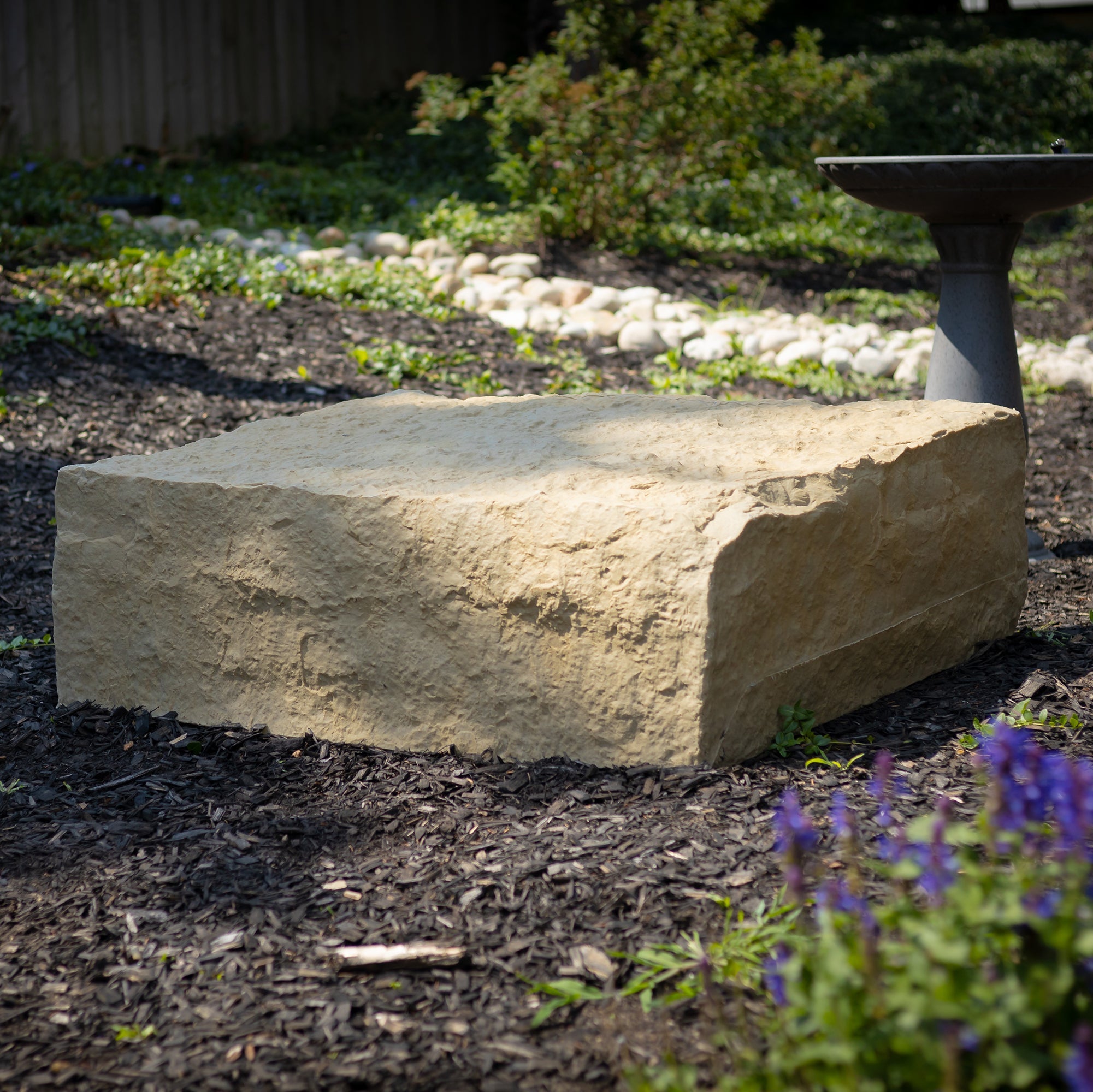 extra large landscape rock in sandstone on wood chips in a garden with bird bath
