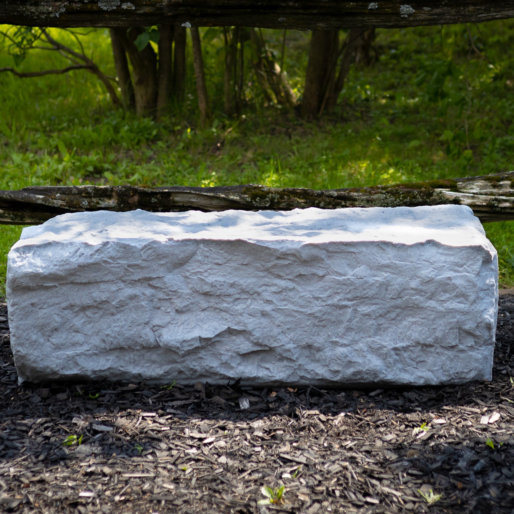 extra large landscape rock in grey on a woodchip garden with wooden fence in background